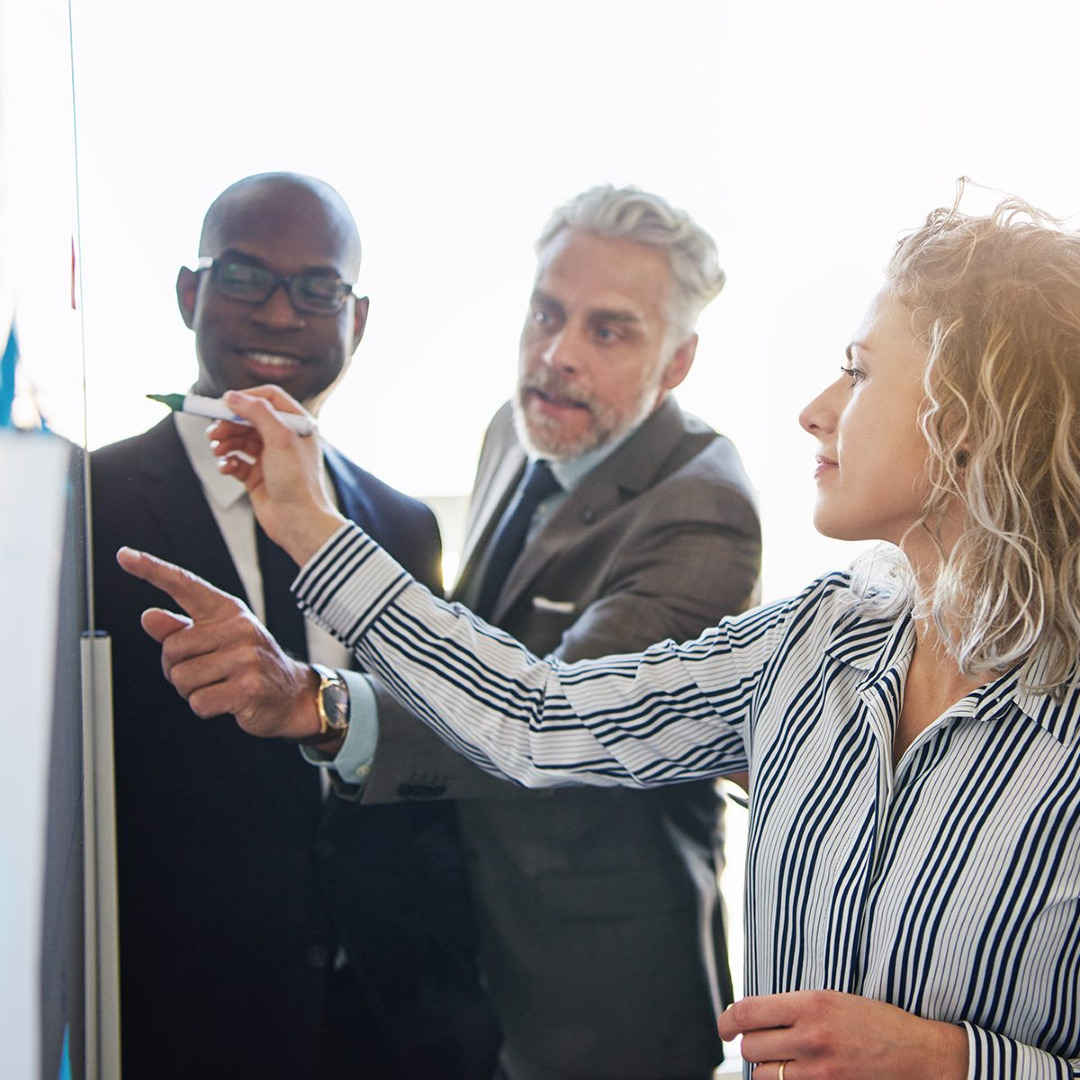 Picture of three coworkers coming up with a strategy on a whiteboard