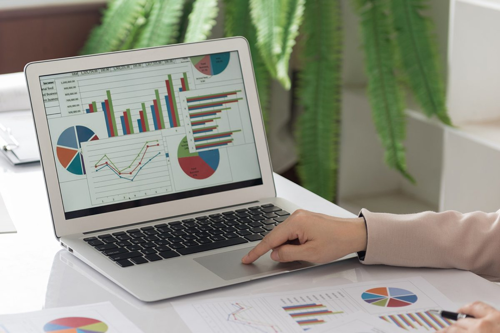 Picture of a person's hand operating a laptop with graphs on screen